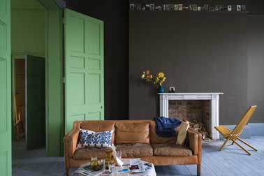 Salon cosy vert et chocolat avec deux peintures Farrow and Ball Une peinture de salon cosy avec une peinture murale chocolat. Mariée ici avec une porte peinte dans un ton vert clair lumineux un canapé en cuir camel et des coussins colorés
