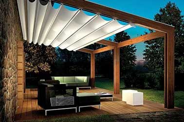 Aménagement d’une terrasse design avec un salon de jardin contemporain et une pergola rétractable sur une structure de cadre en bois et aluminium. Eclairée par une lampe cube extérieure 