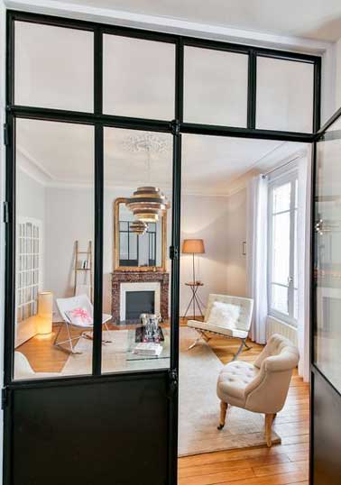Un salon séparé d’une entrée grâce à une verrière d’intérieure. Sa structure métallique est valorisée par parquet et murs blancs et modernise la déco de la pièce 