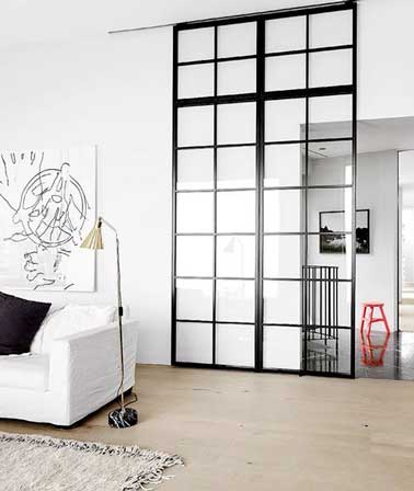 Le salon gagne en intimité avec sa verrière intérieure quadrillée montée sur porte coulissante. En contraste sur les murs blancs, elle impose son style industriel dans le salon