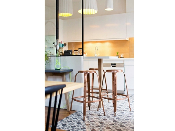 Cette verrière d’intérieur ainsi que le carrelage géométrique viennent séparer avec délicatesse une cuisine moderne et le salon. Une tableau haute le long des vitres est réservée aux petits déjeuners. 