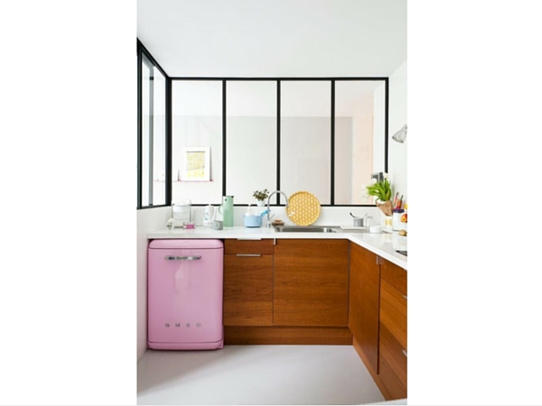 Une cuisine borgne gagne en lumière grâce à l’installation d’une verrière intérieure au style industriel. Elle vient casser le côté très féminin apporté par le réfrigérateur rose vintage en apportant du rythme. 