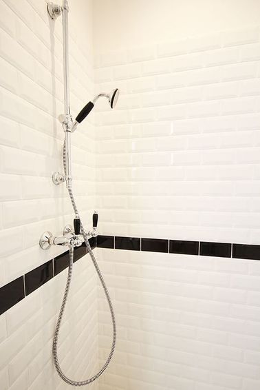 La douche se fait chic et sobre avec un carrelage métro coupé d'une frise noire à hauteur de la robinetterie