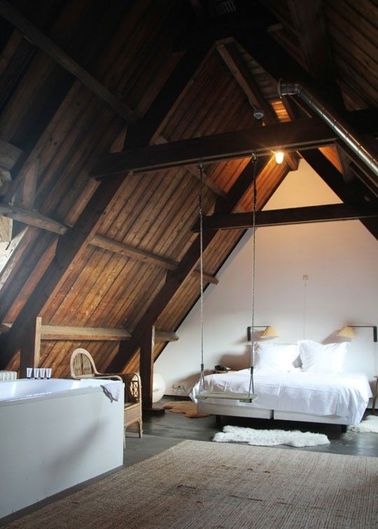 Une chambre avec poutres sous un toit en bois pentu