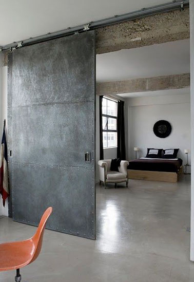 Déco industrielle dans la chambre parentale avec cette cloison coulissante réalisée à partir d’une porte recyclée traitée avec un enduit effet béton pour isoler la chambre du salon