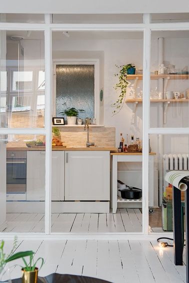 Une cuisine ouverte avec une verrière de séparation Au lieu de conserver la cloison d’origine, on a ouvert cette cuisine blanche avec une verrière intérieure qui agrandit visuellement l'espace dans ce petit appartement.