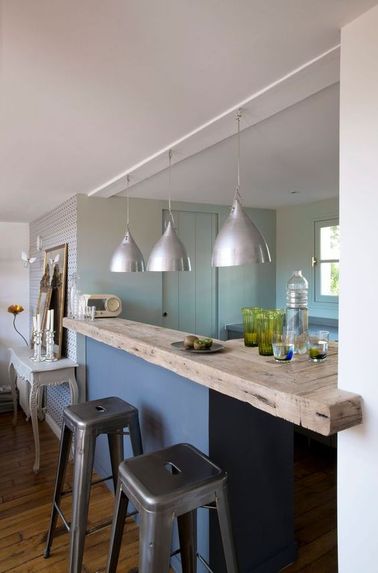 La cuisine s'ouvre sur le salon avec un bar en bois brut Il ne suffit parfois pas de grand-chose pour apporter de la convivialité à votre maison : une cuisine industrielle ouverte permet de continuer la conversation même quand on fait la cuisine.