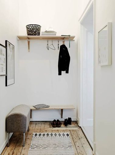Déco épurée dans le hall entrée d’un appartement suédois. Un banc vintage, une étagère basse pour poser ses clés et rangement sur étagère haute avec penderie. 