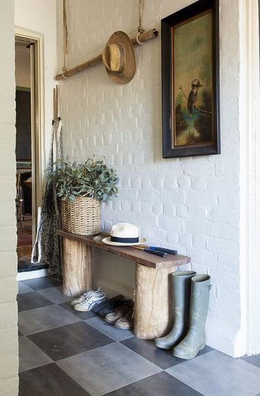 Ambiance déco rustique dans un hall d’entrée en briques blanches avec un banc rangement chaussures fait de 2 rondins et une planche