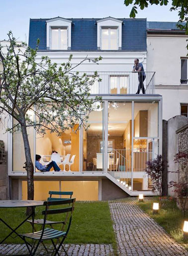 Ici l’extension maison permet d'ajouter un séjour avec une salle à manger et un espace détente. Les grands panneaux de verre donne un coup de jeune à la façade ancienne.