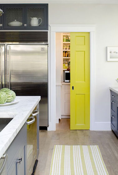 Une cloison coulissante jaune pétillante colore la cuisine ouverte et ferme un placard de rangement dans une déco contemporaine. Assortie au tapis de sol elle est valorisée par les murs blancs