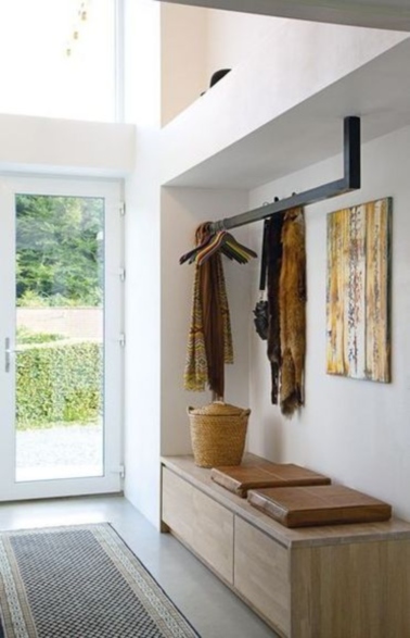 Un hall d’entrée lumineux grâce à la porte d’entrée en verre et rangement optimisé avec un meuble bas placé dans une alcôve et une barre en fer pour suspendre les vêtements.