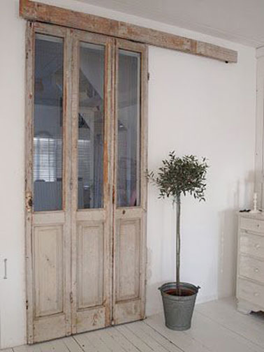 Une cloison coulissante confectionnée à l'aide d'une porte fenêtre en bois patinée inspire une déco provençale dans cette entrée blanche. Mixée avec un parquet blanc lazuré elle structure l'espace
