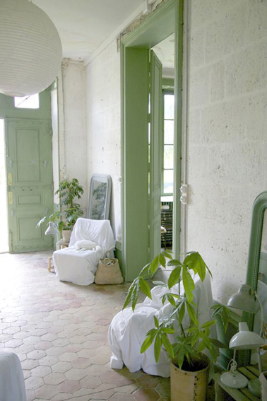 Voilà l'entrée d'une ancienne maison au sol en tommettes rajeunit grâce à une couleur peinture vert d'eau, des miroirs de récup et des fauteuils drapés de tissu blanc. 