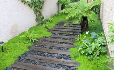 Pas japonais fait avec des traverses en bois de recup sur du gravier noir, pour aménager l'allée du jardin dans une ambiance tropicale avec la mousse et les fougères.