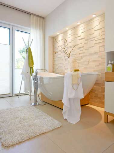 Une salle de bain zen et lumineuse avec un carrelage sol beige clair assorti aux pierres en parement du mur de la baignoire îlot montée sur socle bois.