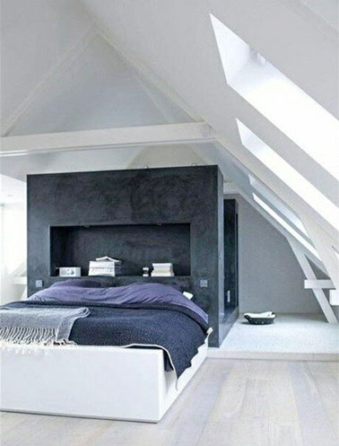 La tête de lit fait office de cloison avec la salle de bain et sert d'étagère dans cette suite parentale blanche et lumineuse prenant place sous les combles 