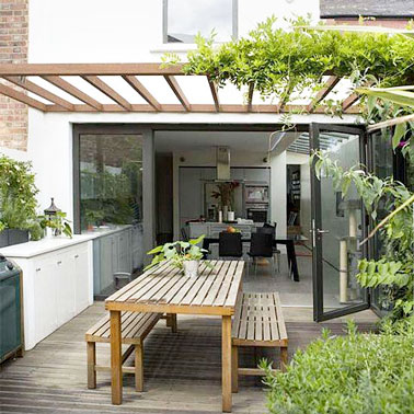 Une cuisine d'été qui s'orne d'une pergola végétale afin de faire de l'ombre et d'aménager un cocon original et intime dans le jardin. Une terrasse bois charmante et conviviale 