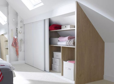 Un dressing sous pente en bois et blanc, à portes coulissantes, monté sur les parties basse des combles d’un studio, bien insérée et apporte une touche de déco à la chambre.