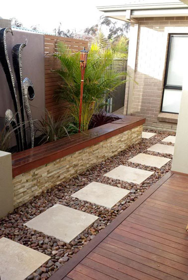Une élégante allée de jardin fait à partir de pas japonais composé de pavés de pierre blanc cassé sur du gravier de cailloux sombres en accord avec la déco de la terrasse.