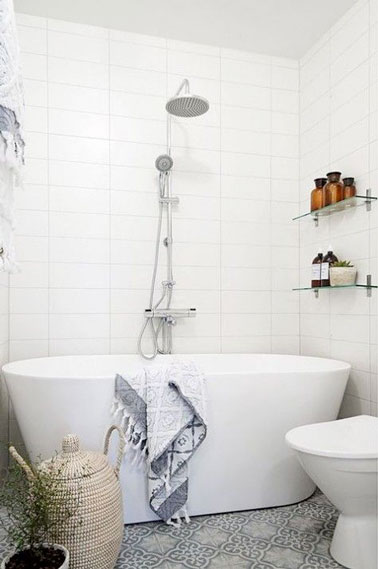 Aménagée avec une baignoire îlot, cette petite salle de bain au sol en carreaux de ciment est fonctionnelle est déco grâce à des étagères pratiques fixées au mur 