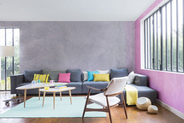 Un salon chic avec un mur peint en rose et une peinture couleur parme recouvrant un autre mur. Une déco pimpante soulignée par des coussins colorés et le parquet