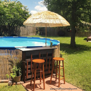 Voilà une déco agréable qui invite au voyage autour de la piscine avec un petit bar décoré d'un parasol exotique et des canisses qui cachent la toile de la piscine ! 