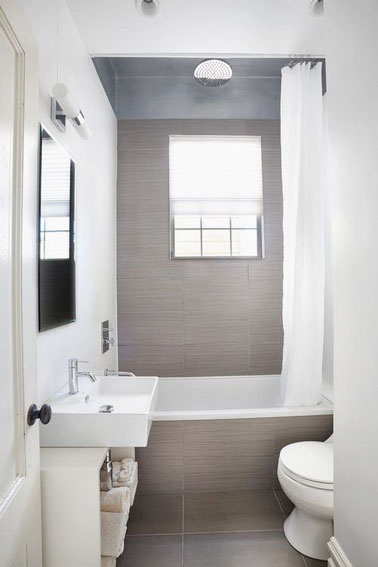 Apaisante et ultra lumineuse, cette petite salle de bain grise est 100% optimisée avec sa petite baignoire aménagée au fond de la pièce et un meuble de rangement pratique 