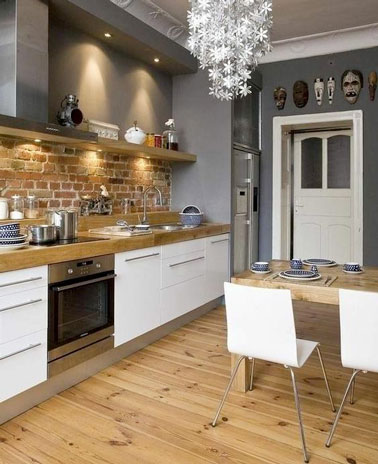 Une touche rustique s'est invitée dans la déco de cette cuisine conviviale avec un mur en brique en crédence souligné par un plan de travail en bois et un beau parquet 
