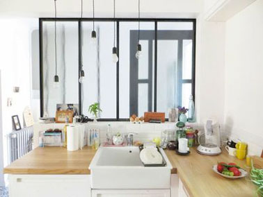 Une cuisine avec vue sur l’entrée grâce à l’aménagement d’une verrière intérieure dans cette charmante petite cuisine blanche au plan de travail en bois