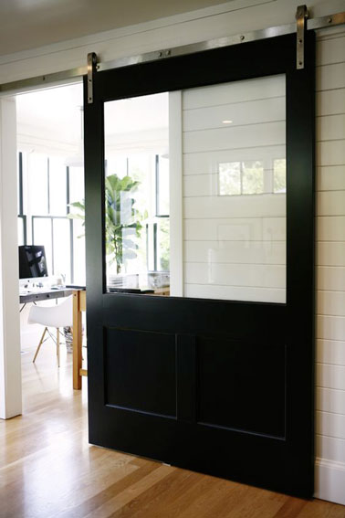 Cette porte coulissante en bois peinte en noir et agrémentée d'une grande vitre permettant de faire passer la lumière, embellit la déco de cette maison d'architecte 