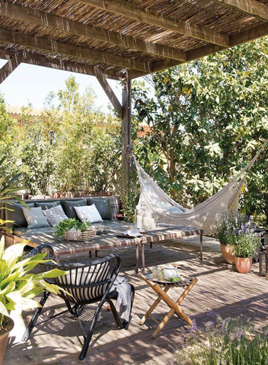 Hamac, fauteuil de jardin ou canapé, les choix ne manquent pas pour se détendre sur cette terrasse cosy entourée de verdure prenant place sous la pergola ! 