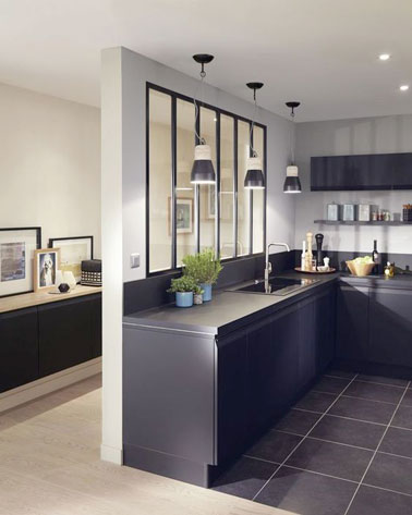 Cette cuisine design noire semi ouverte est lumineuse et charmante grâce à une verrière intérieure qui laisse entrer la lumière et sépare le couloir de la cuisine 