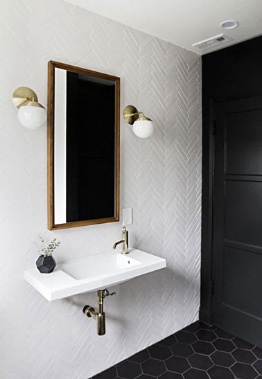 Style vintage dans cette jolie salle de bain blanche au sol en tommettes de couleur noir décorée d'un beau miroir et de deux appliques murales blanches et dorées 