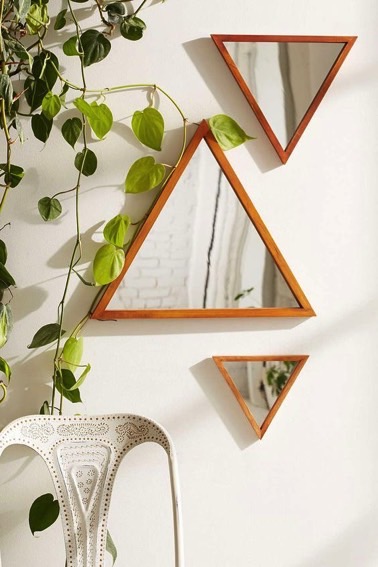 Des petits miroirs en formes de triangles sont joliment disposés sur un mur blanc de façon déco afin de donner du dynamisme et un certain cachet à la pièce 