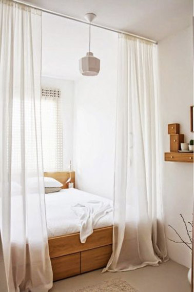 Le lit placé dans un recoin de cette chambre parentale blanche et bois constitue un espace bien délimité par des voilages afin de créer un espace intime à part 