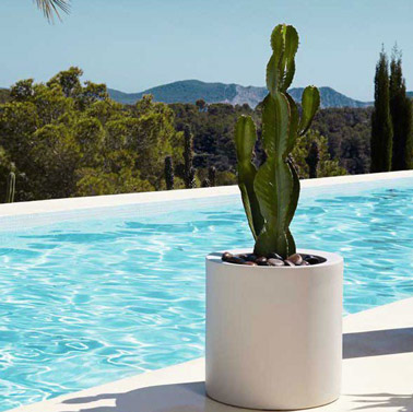 On opte pour un pot de forme cylindrique pour décorer la piscine avec classe ! De couleur blanc, il accueille un cactus et des galets pour un effet déco top 