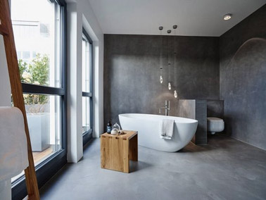 Déco zen et style épuré dans la salle de bain avec les murs et le sol en béton ciré, une baignoire îlot, un tabouret en bois et des suspensions lumineuses originales 