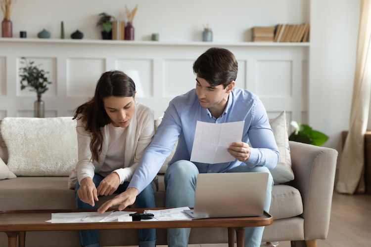 Couple dans un canapé en train de faire les comptes pour économiser de l'argent dans une maison