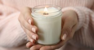 Femme tenant une bougie parfumée et allumée dans ses mains avec un gros pull.
