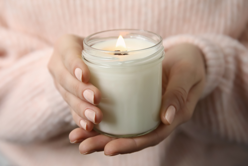 Femme tenant une bougie parfumée et allumée dans ses mains avec un gros pull.