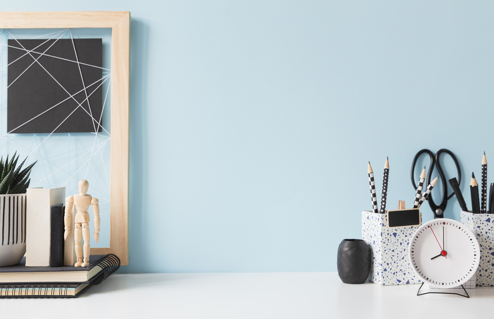 bureau blanc et un mur bleu ciel, avec des pots à crayons et une petite plante